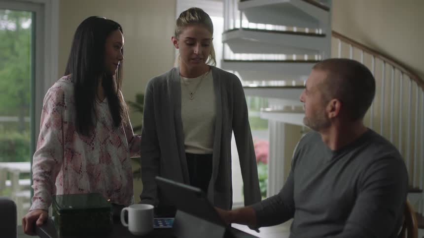 Man working at home sitting at a desk talking with two young woman