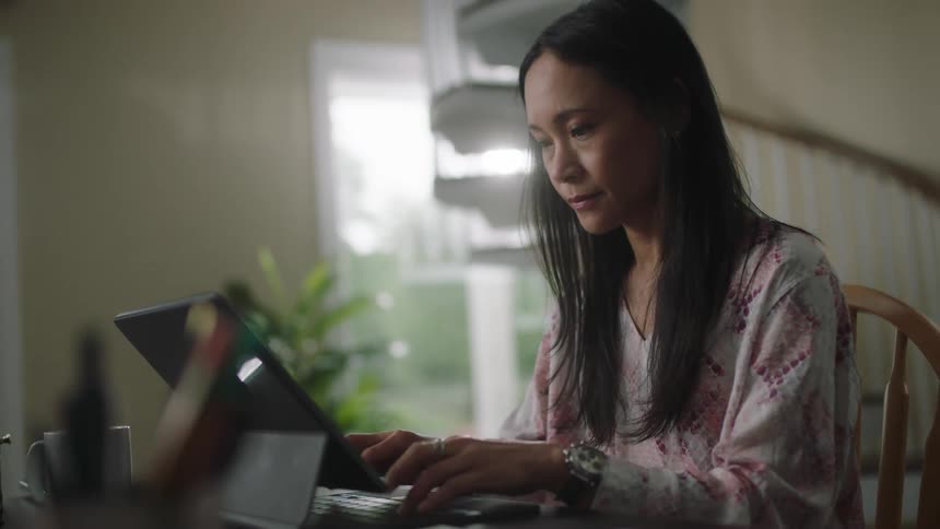 Young woman sitting on a desk at home typing on a laptop