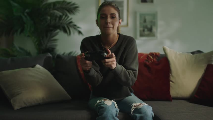Woman sits on sofa playing game with game controller