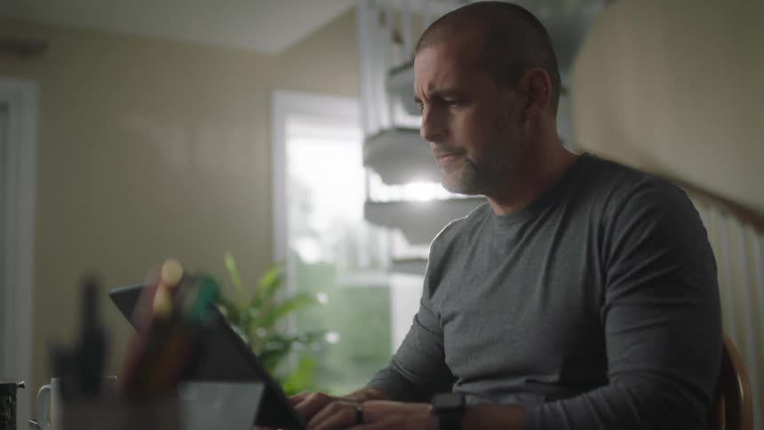 Man sits at desk near spiral staircase typing on laptop