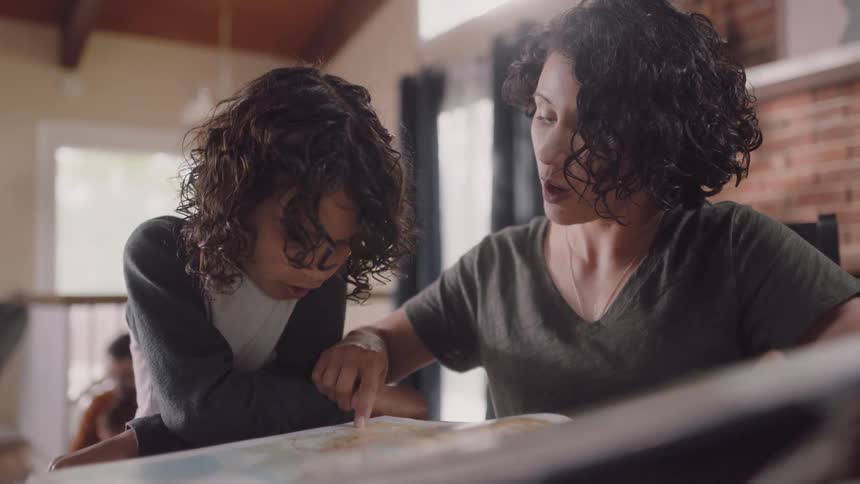 Mother and child study atlas while father sits with other son at table