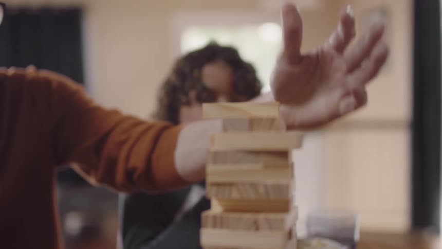 A man places a piece on a jenga game as his son eats popcorn and his wife points