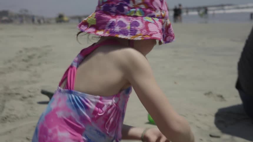 Little girl digging in the sand with a shovel on a beach