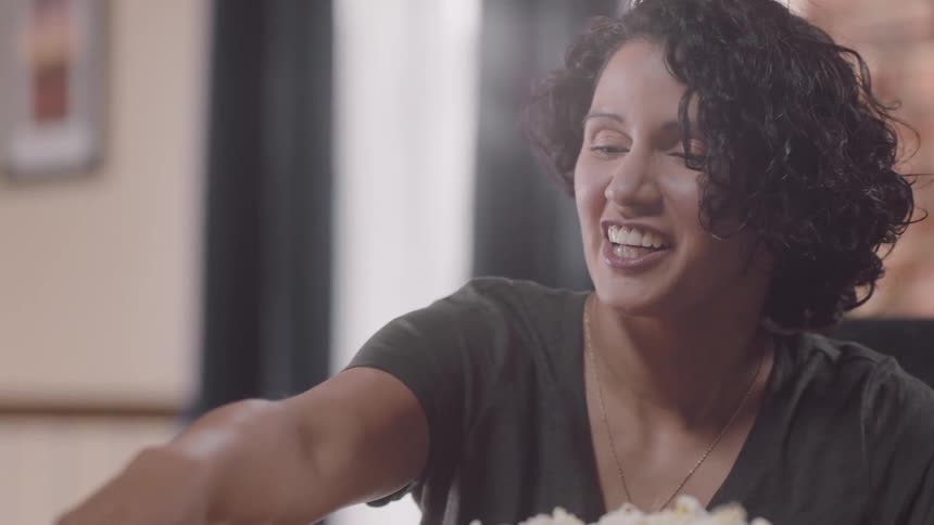 Parents playing jenga with their kids on a table at home while eating popcorn