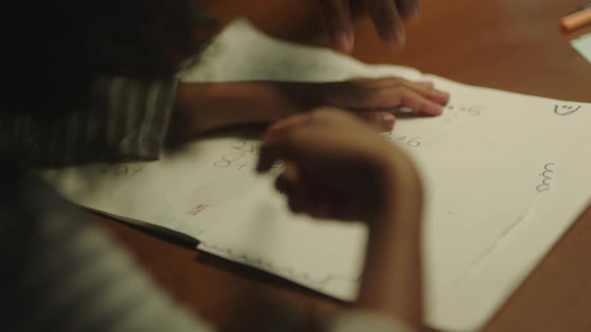 A child is writing her homework with a pencil