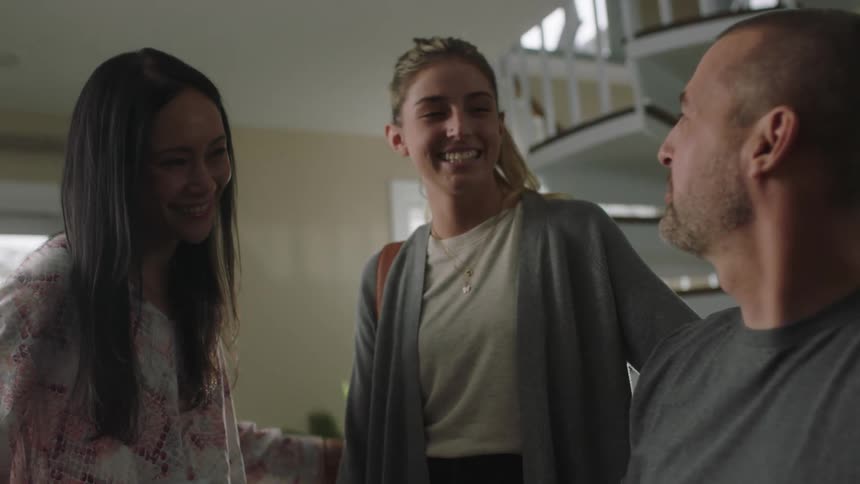 A few people are laughing and talking in a house near a staircase