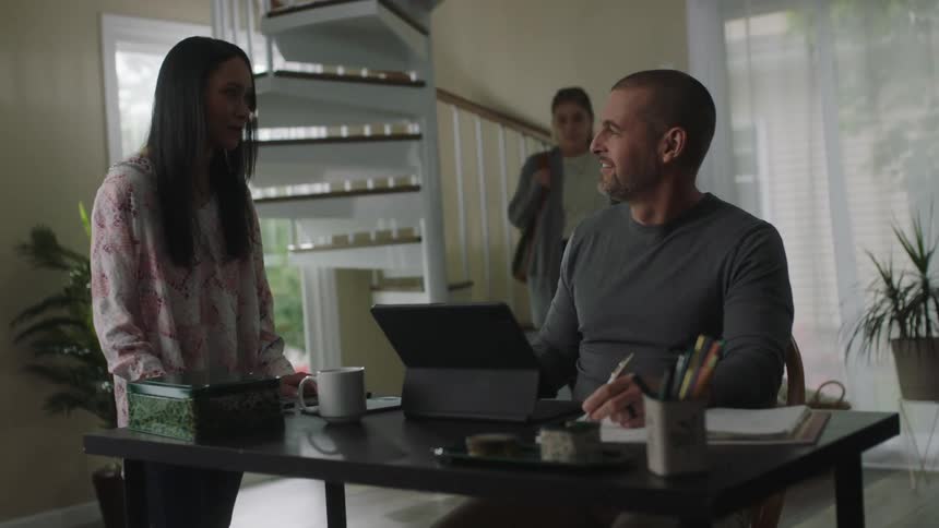 Man sitting at a desk at home talking with a girl while a teenager walks down the stairs