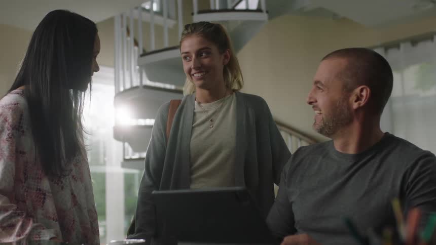 A girl shakes her head and ponytail while talking and laughing with a man and woman
