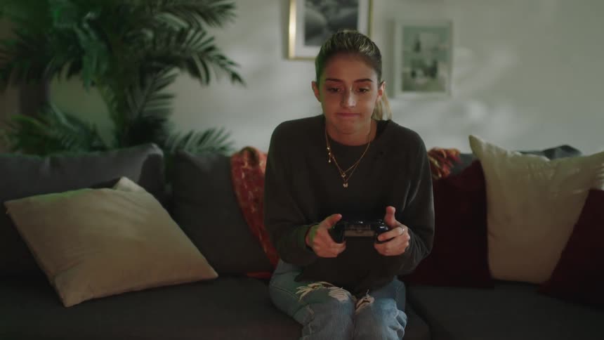 A girl bites her lip and slaps her hand in frustration as she plays a console video game with a controller