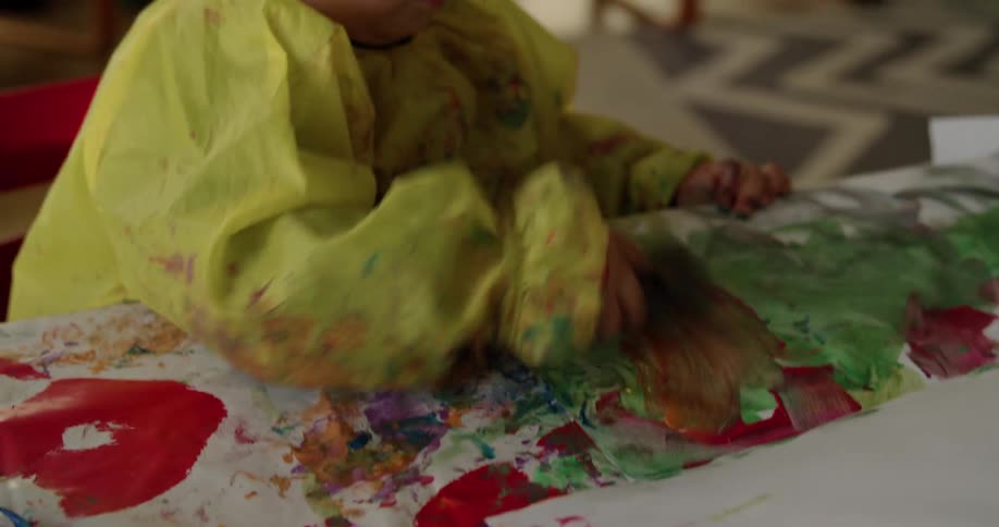 Girl wearing yellow plastic clothes painting on paper with colorful paints at home