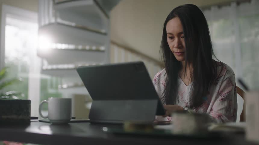 Young woman sitting at a desk at home typing on a laptop in the morning