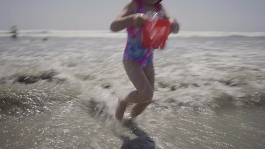 A girl fills her pail with water and runs back on the beach