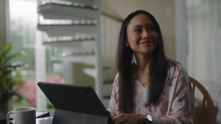 A woman typing on a tablet while another woman walks by