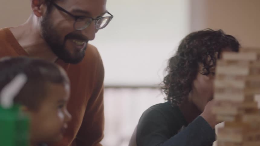 Parents cheer on their son as he places a piece on a wooden block game