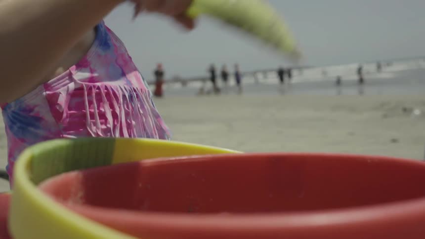 A girl shoves sand into a bucket on the beach