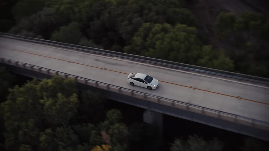 Aerial view of a white car driving over an overpass in the countryside