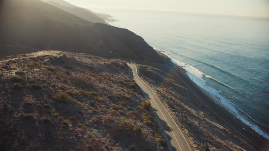 An aerial view of a coastline with a mountain and highway in the morning
