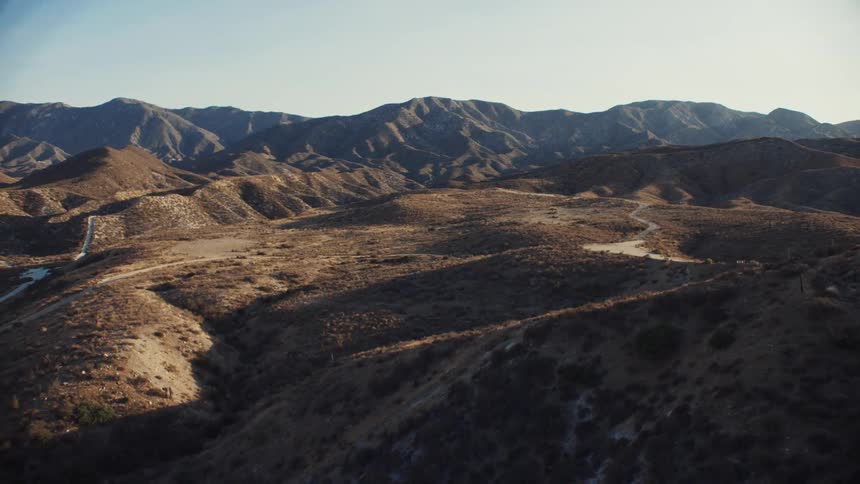 Aerial view of dirt roads over the hills near the mountains at morning