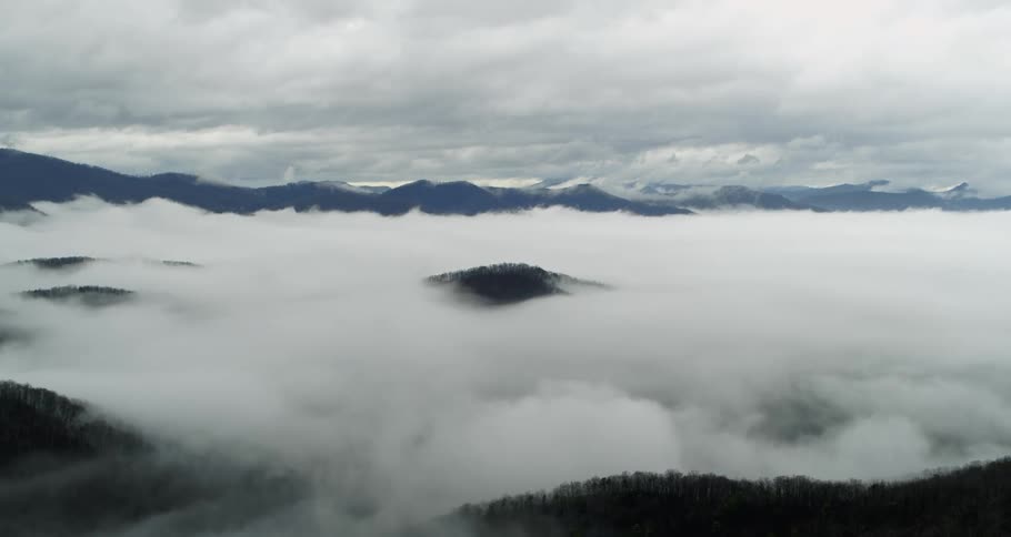 Clouds move over mountains covered with trees high in a cloudy sky