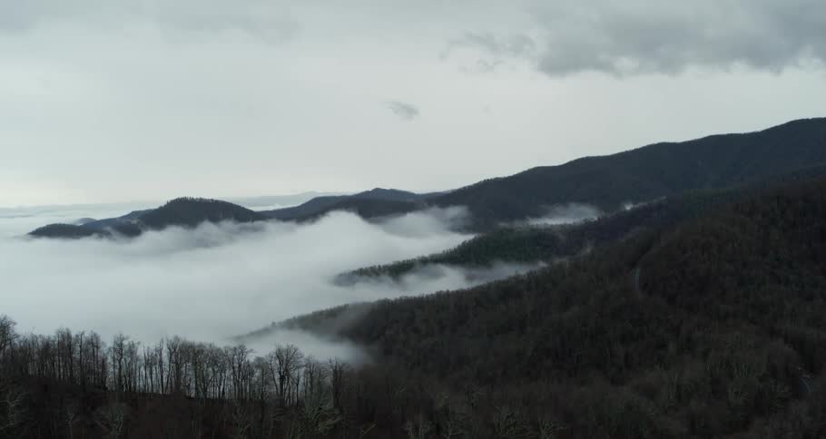 Aerial view of white clouds over the forest in the mountain slopes at evening