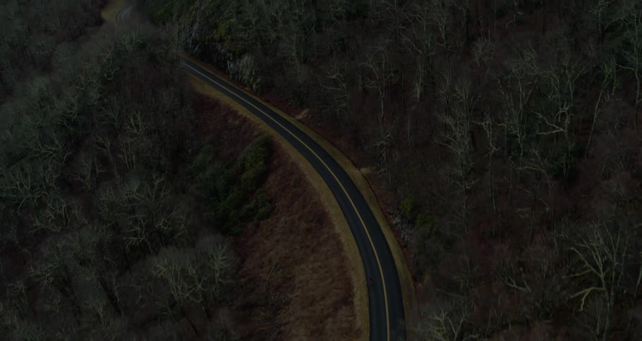 Aerial view of mountain highway on the slope with distant mountains surrounded by clouds