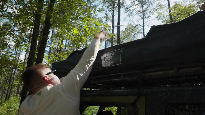 son helps father unpack a tent from the roof of a car in the forest at morning