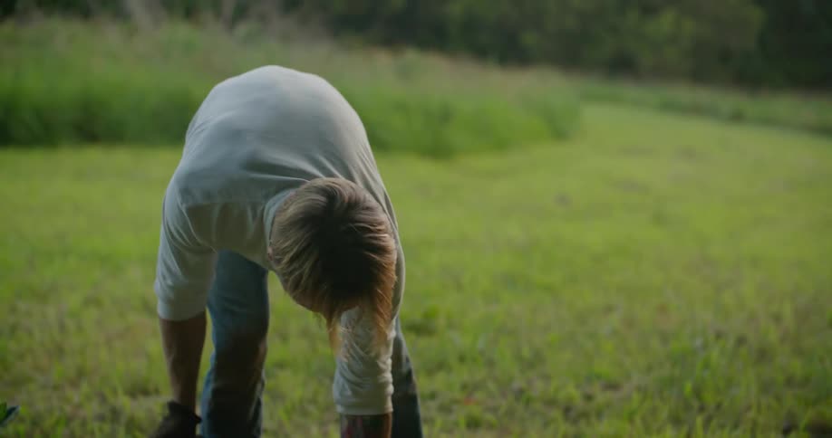A man is digging a hole in a grassy field in a woodland area during the daytime