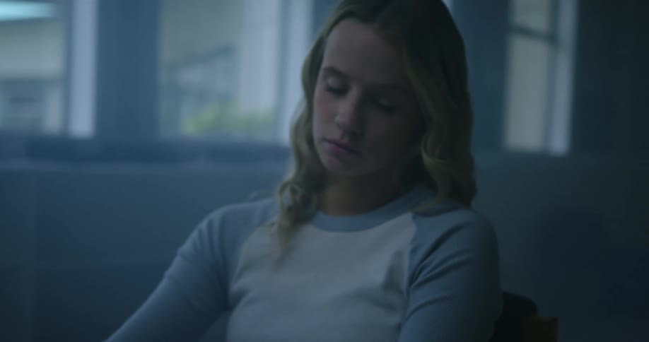 Young tired bored blonde girl reading a book inside a dimly lit classroom