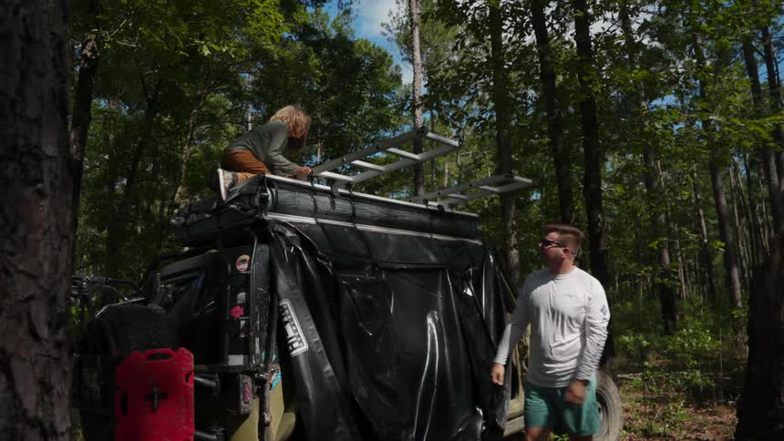 Father and son extending ladders over a jeep while camping in the forest