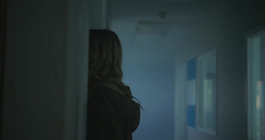 A teenager holds a stack of books in her arms while standing in a school hallway