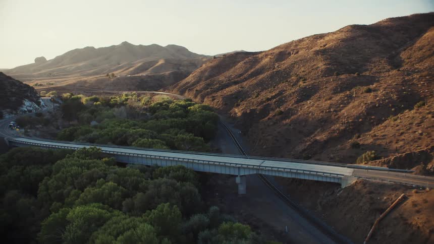 A train travels along the side of mountains and under a highway