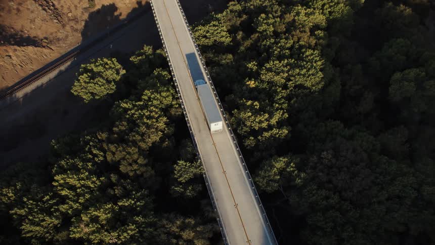 A semi truck drives across a long narrow bridge over a forest