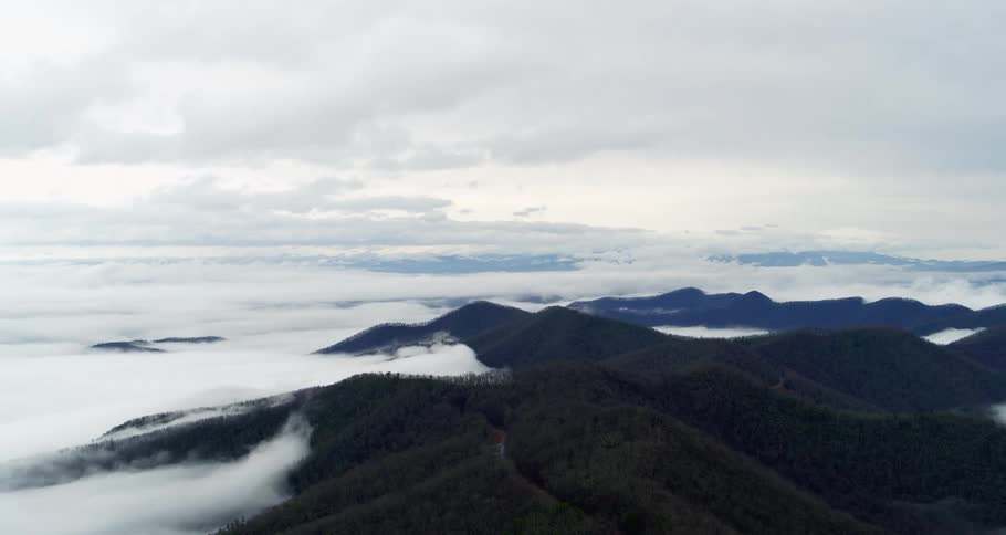 Clouds move over mountains covered with trees high in a cloudy sky