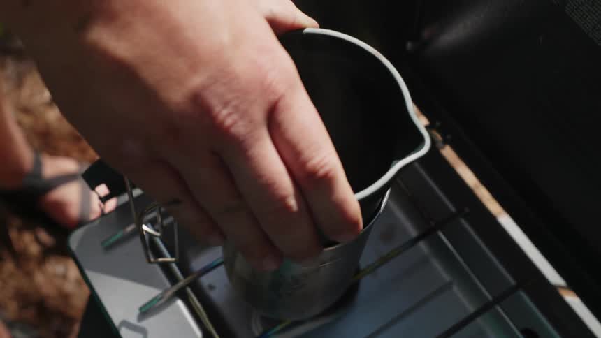 A man is preparing coffee on a camp stove outdoors during the day