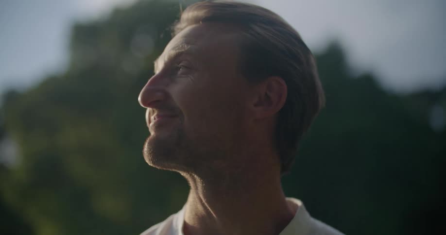 A man is standing outside running his hands through his hair and smiling