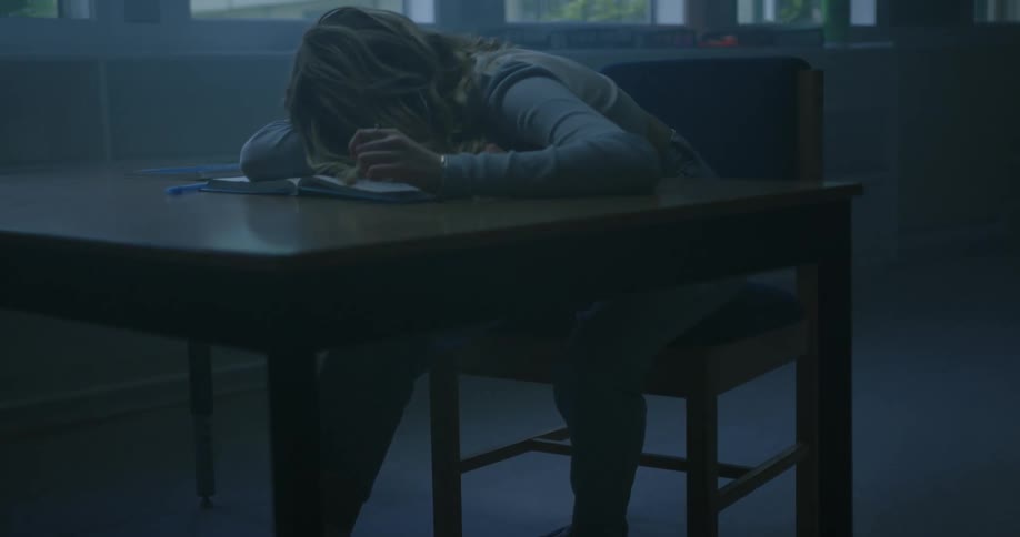 A student is sleeping at the desk in the dark class