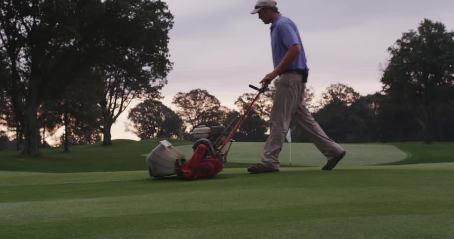 A man is pushing a lawnmower on a golf course