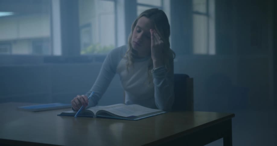 Woman sits at table looking tired while studying textbook