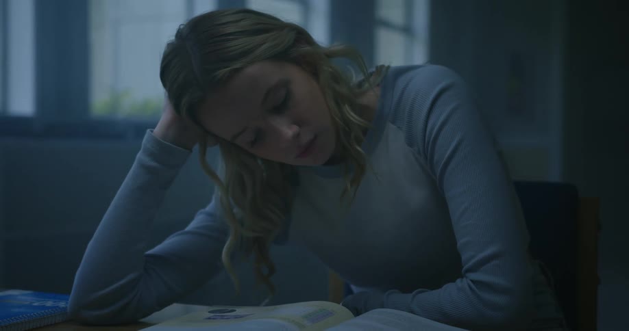 Blonde girl with light blue sweatshirt sits at desk and reads books