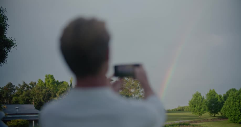 A man using a smartphone to take photos of a rainbow