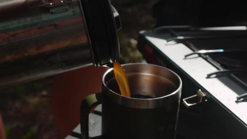 A man pours coffee from a thermos into a cup while outdoors