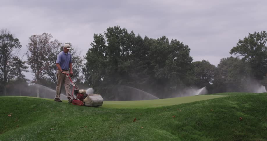 A man is mowing a grass covered hill on a golf course