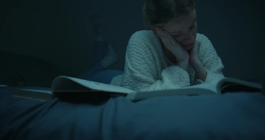A young woman rubs her eyes as she struggles to stay awake while studying in bed