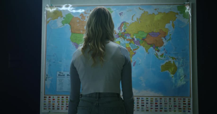 The back of a woman standing staring at a hanging world map