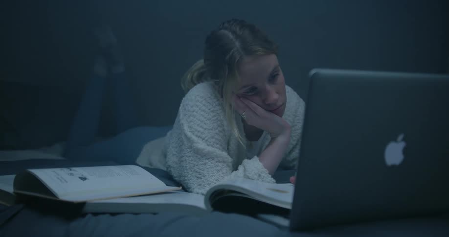 A girl is laying in bed bored while studying