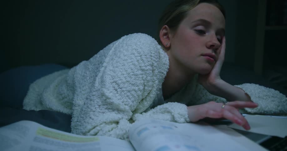 Tired teenage girl almost falling asleep in front of a laptop studying in bed