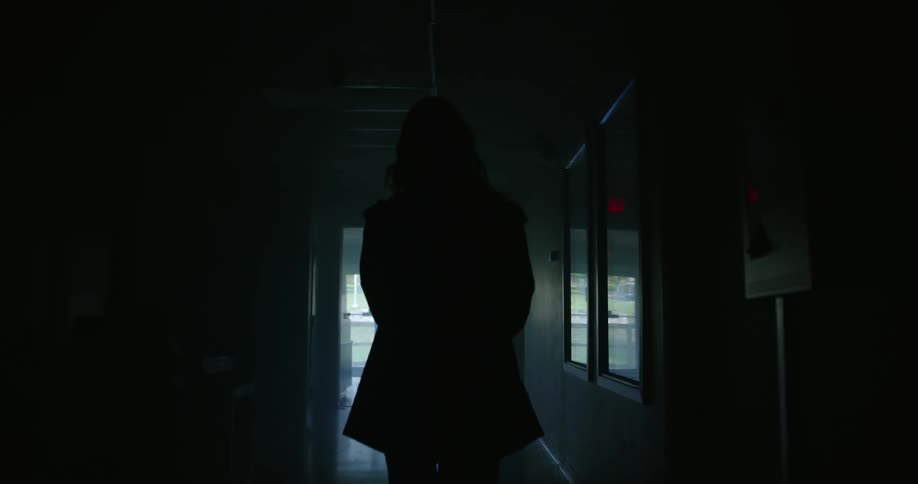 A woman walks down a long dark hallway in a building