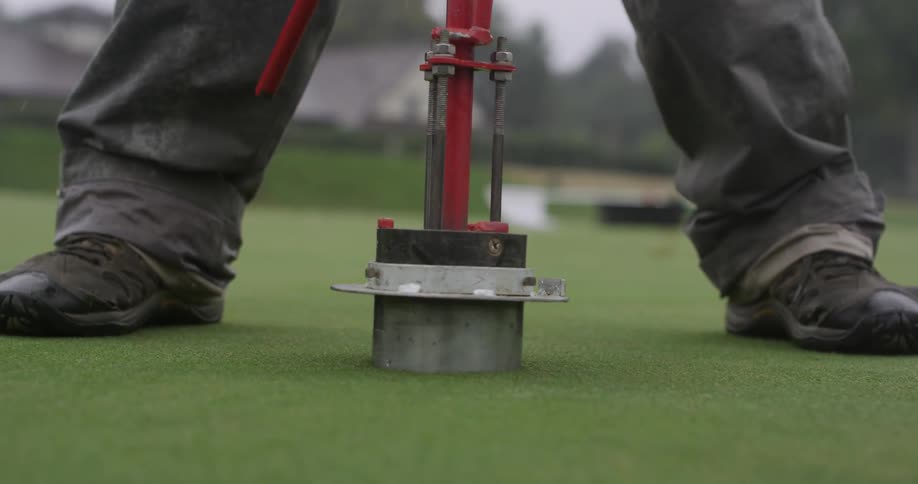 Person putting a golf hole cutter in the ground