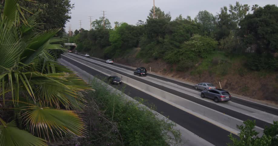 Cars drive down a road with hills on both sides