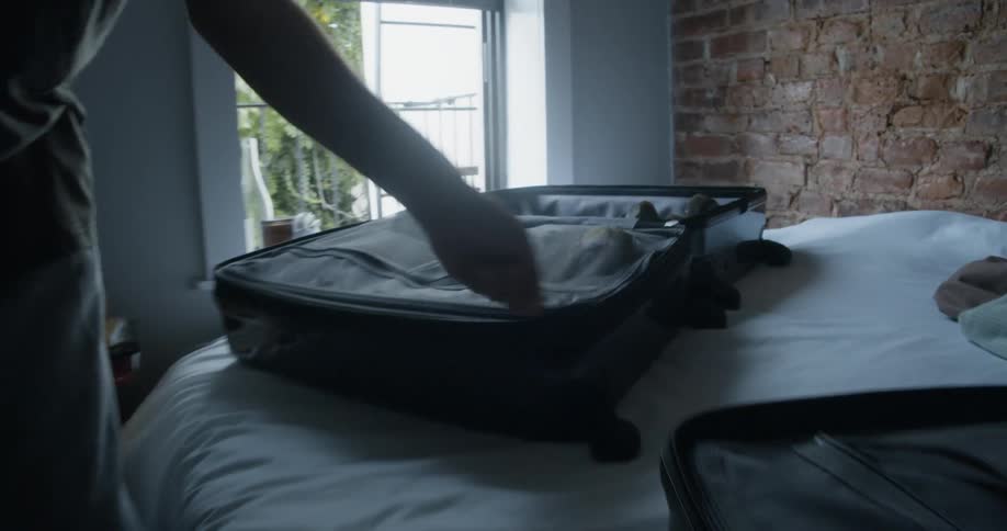 Man closes inner zipper in suitcase sitting on bed